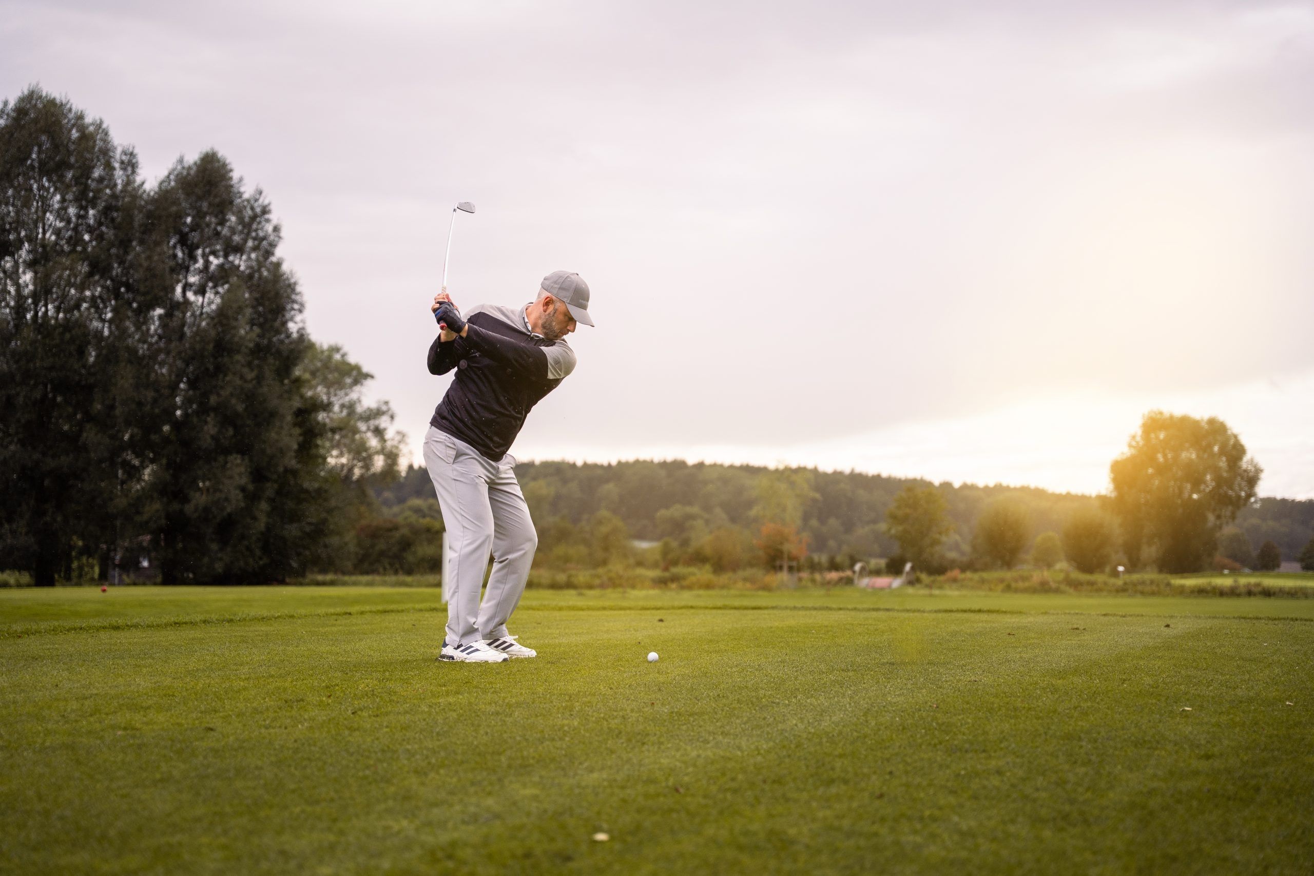Ein Mann spielt Golf auf einem gruenen Feld bei Sonnenuntergang.